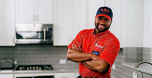 Smiling Mr. Rooter technician standing in a kitchen with his arms crossed.