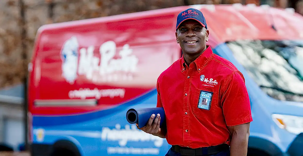 Smiling Mr. Rooter technician standing in front of a branded van.